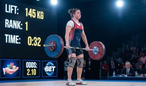 Professional weightlifter on stage with competition scoreboard and betting symbols